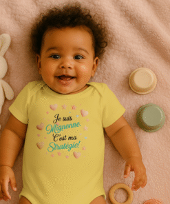 Bébé souriant en body humoristique jaune “Je suis mignonne, c’est ma stratégie !” allongé sur une couverture avec un doudou lapin